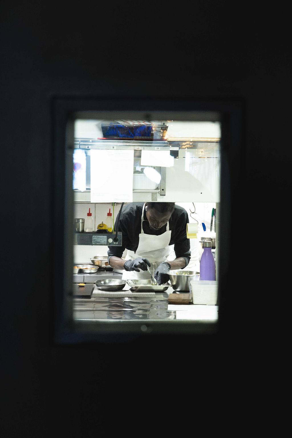 A chef plating a dish, seen through the pass