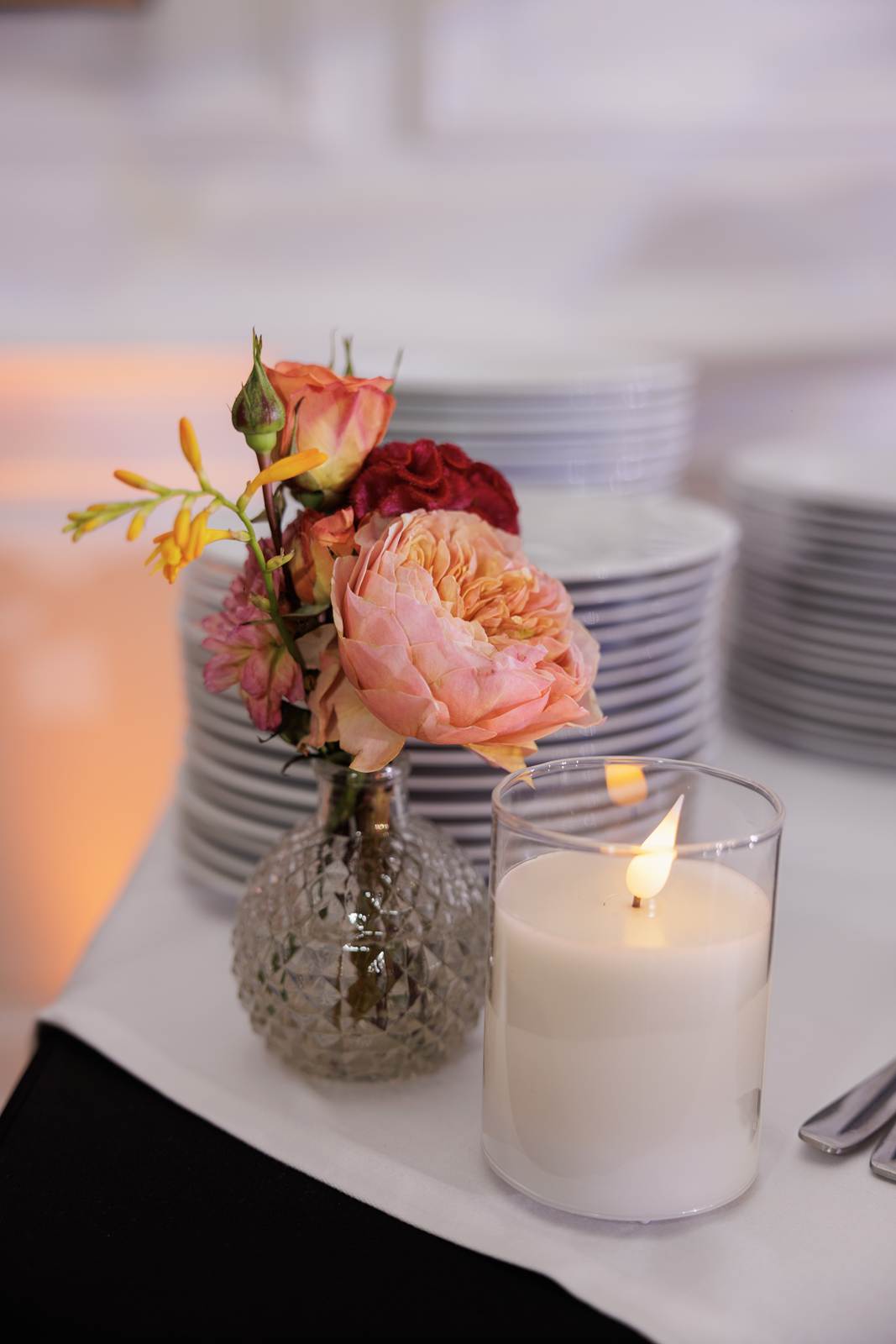 A small posy of roses and a candle before stacks of plates
