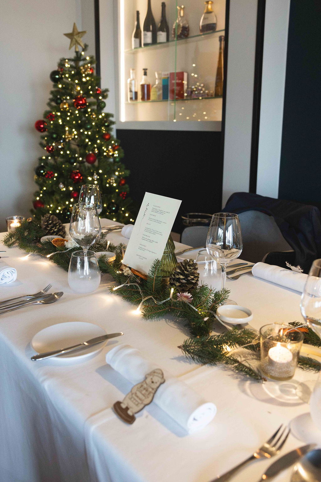 A table laid for a winter dinner, with its menu, candles and a lit Christmas tree